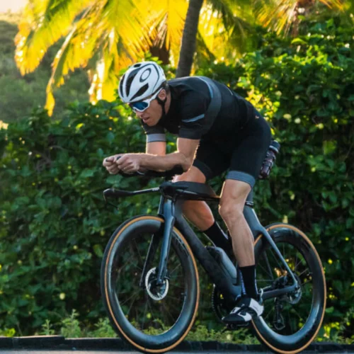 a bicycle rider dressed in black lycra wearing an white oaky crash helmet and white Oakley glasses riding a black TT Aero Bicycle with Enve SES 7.8 aero wheels.