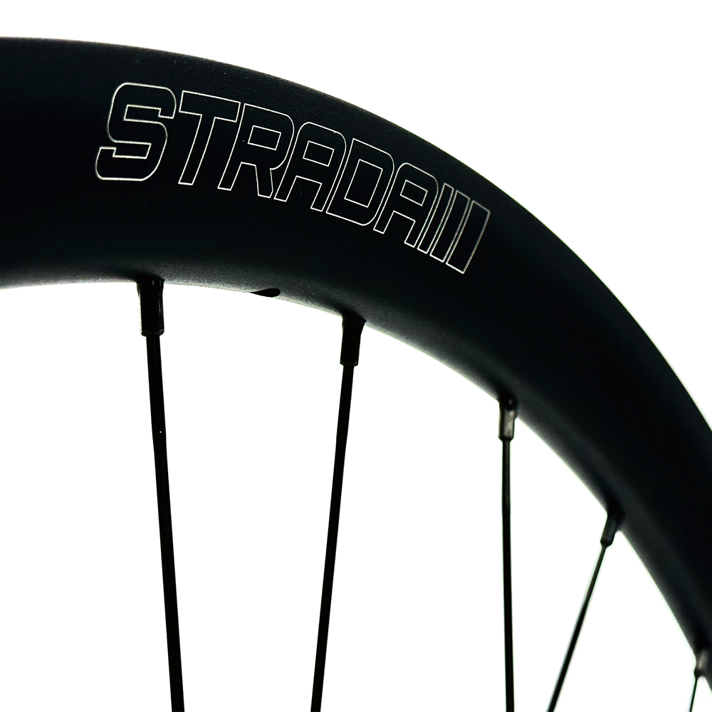 A close up of a black aluminium bicycle rim with the Strada Logo laser etched into it.