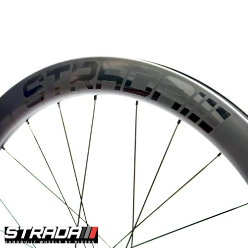 An Image showing a close of the raw carbon finished rim of a Strada PAD 55 Track Ultimate with a black Strada Logo.