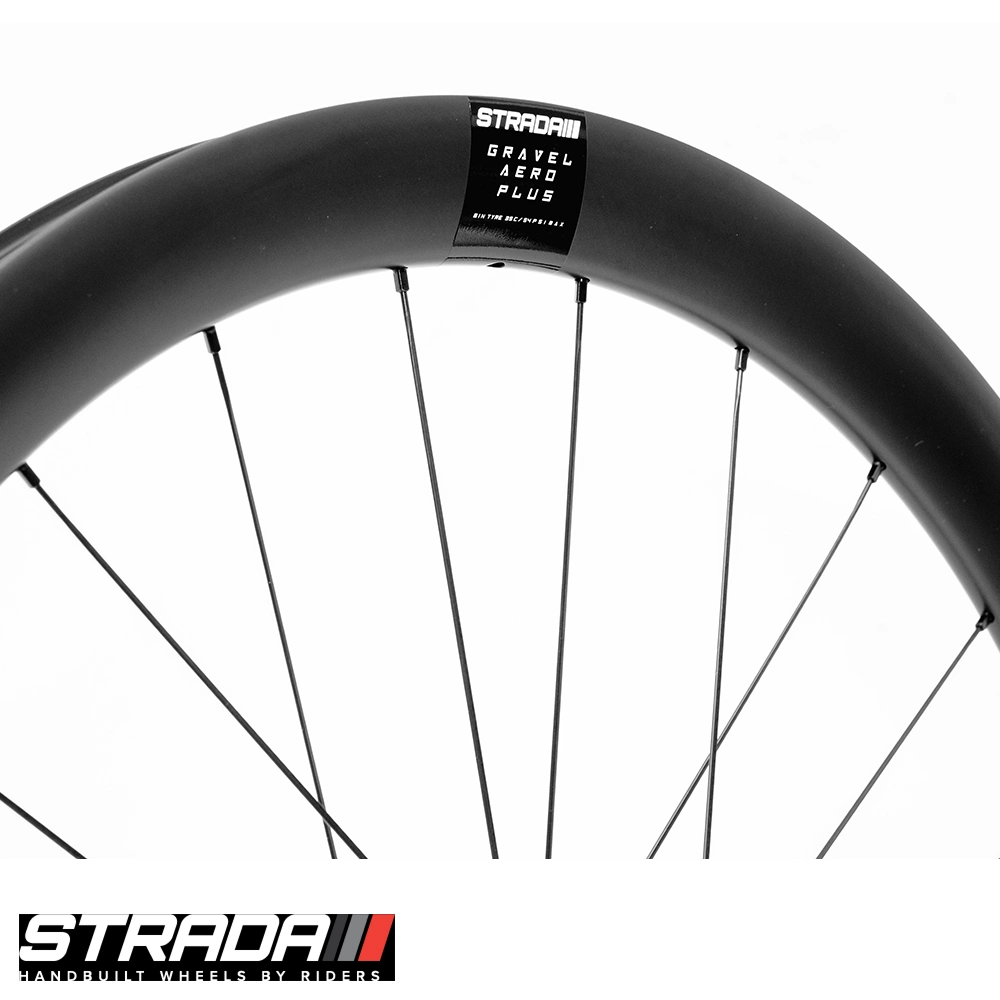 Close-up of Strada Gravel Aero Plus matte black carbon rim showing product label and black spokes on white background